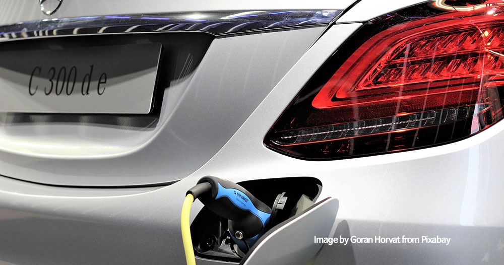 Rear of a silver Mercedes (C300de) being charged, blue charging plug connected to the port with a yellow cable, red taillight visible